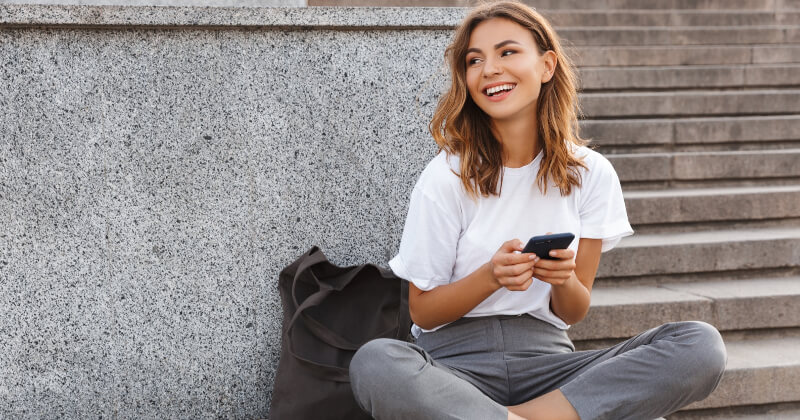A young millennial sitting in front of a building using her phone